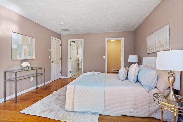 bedroom featuring connected bathroom, baseboards, and wood finished floors