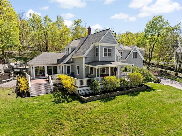 rear view of property featuring roof with shingles, a yard, a chimney, and a deck
