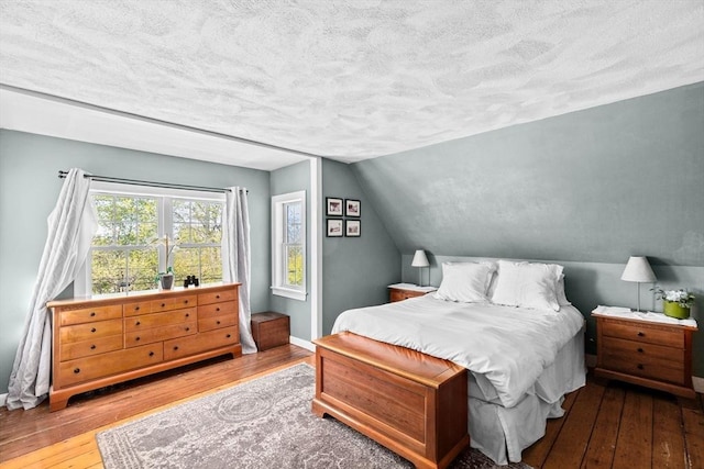 bedroom featuring a textured ceiling, baseboards, hardwood / wood-style floors, and lofted ceiling