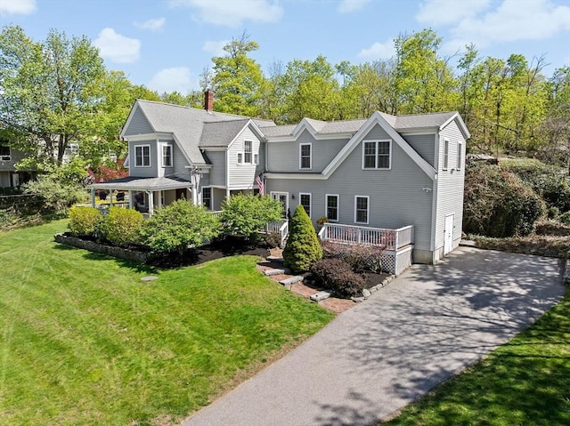 view of front of house featuring driveway, a chimney, and a front lawn