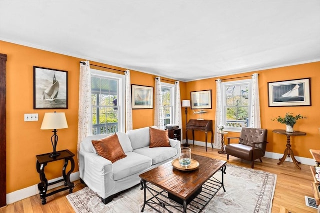 living room with baseboards, ornamental molding, visible vents, and light wood-type flooring