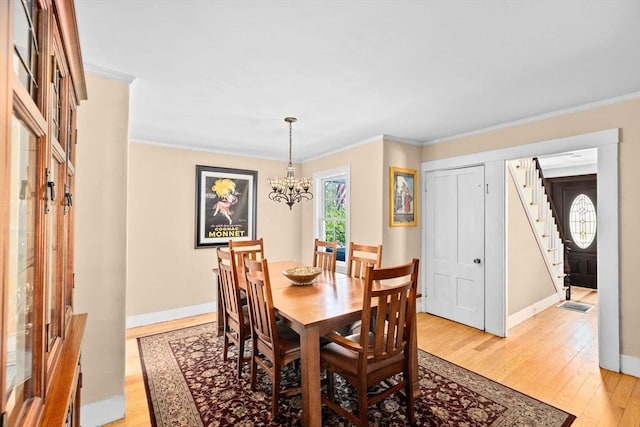 dining room featuring an inviting chandelier, ornamental molding, light wood finished floors, and stairs