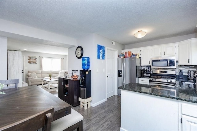 kitchen featuring dark wood-style flooring, a textured ceiling, white cabinets, dark stone countertops, and appliances with stainless steel finishes
