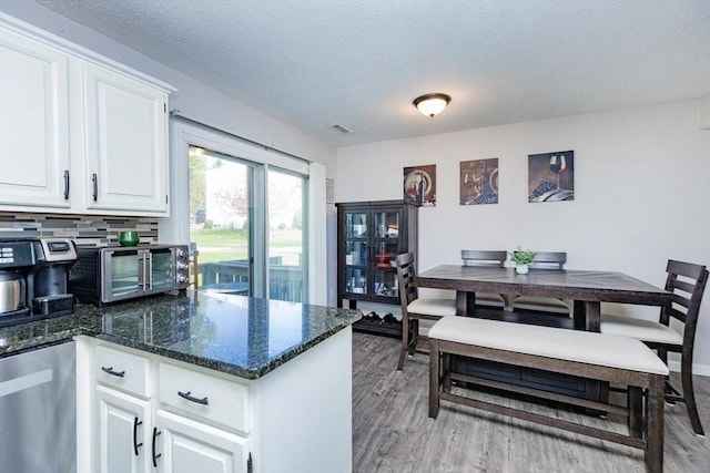 kitchen with white cabinets, a textured ceiling, dark stone countertops, light wood-type flooring, and a toaster
