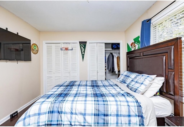 bedroom with two closets, baseboards, and wood finished floors