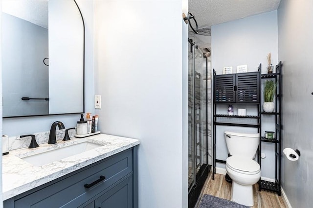 full bath with a textured ceiling, a stall shower, wood finished floors, vanity, and toilet