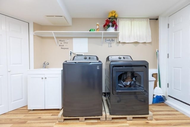 clothes washing area with cabinet space, washing machine and dryer, a sink, and light wood-style floors