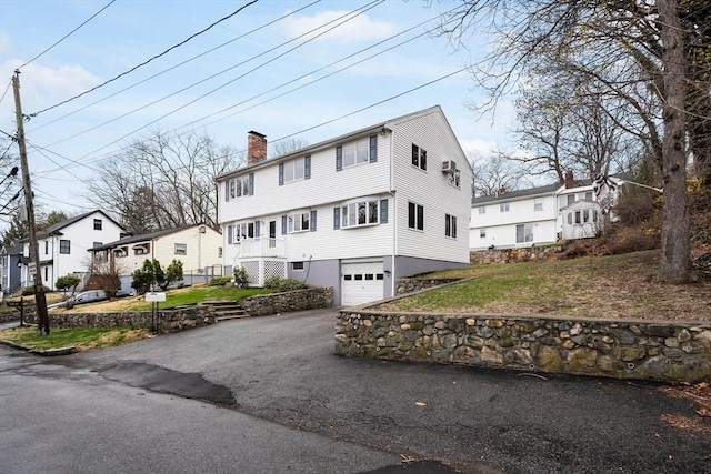 view of front of home featuring an attached garage, a chimney, a front yard, and aphalt driveway