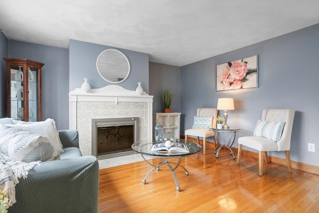 sitting room with a tile fireplace, baseboards, and wood finished floors
