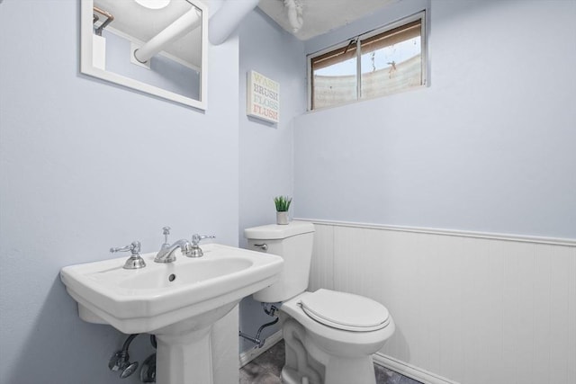 half bath featuring wainscoting and toilet