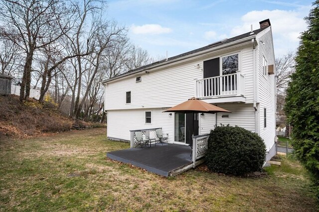 rear view of property with a balcony, a chimney, and a lawn