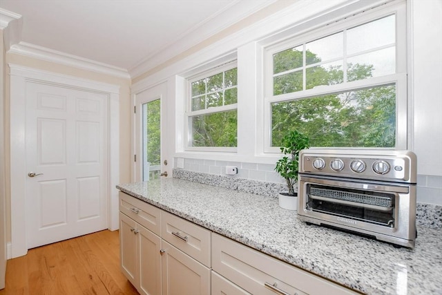 kitchen with light stone counters, white cabinetry, ornamental molding, and light wood-type flooring