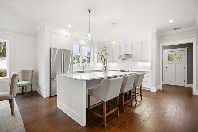 kitchen featuring high end refrigerator, dark wood-type flooring, an island with sink, and white cabinets