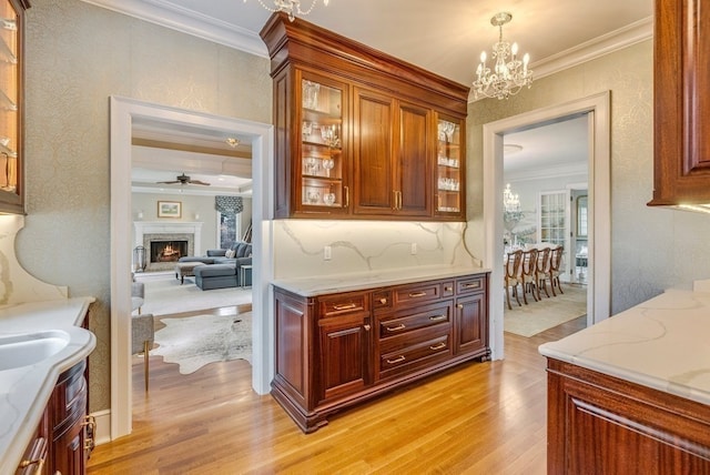 kitchen with light stone counters, crown molding, light hardwood / wood-style floors, and ceiling fan with notable chandelier