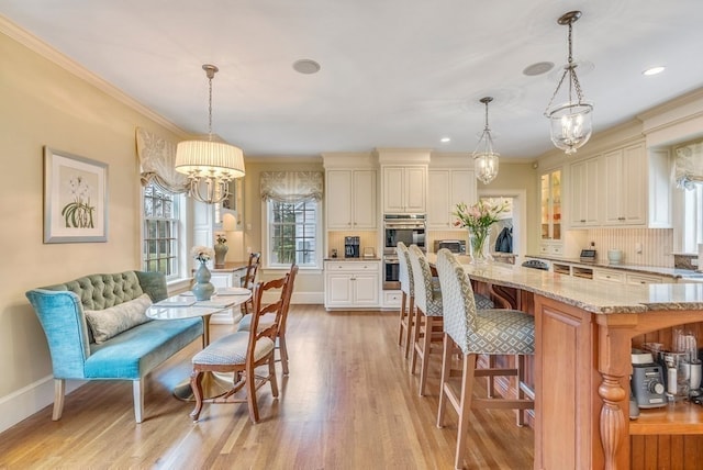 kitchen with pendant lighting, light wood-type flooring, light stone counters, a notable chandelier, and double oven