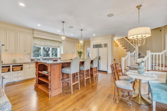 kitchen with paneled refrigerator, hanging light fixtures, light hardwood / wood-style floors, and light stone countertops