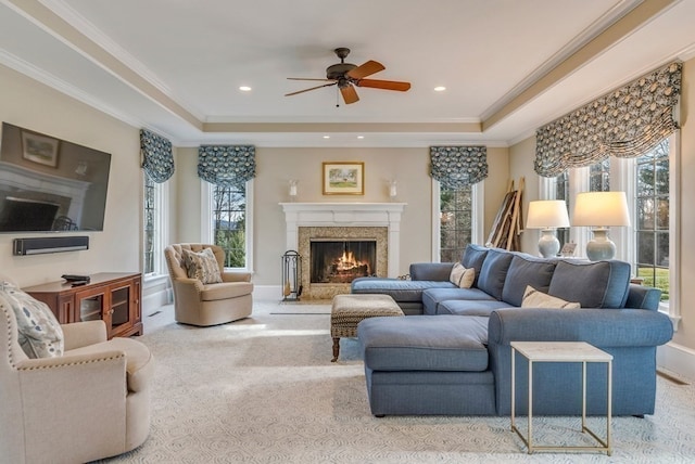 carpeted living room with a premium fireplace, a raised ceiling, ceiling fan, and a wealth of natural light