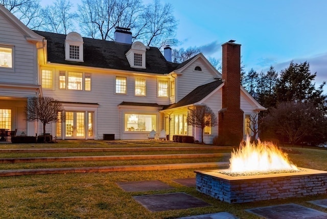 back house at dusk featuring a lawn