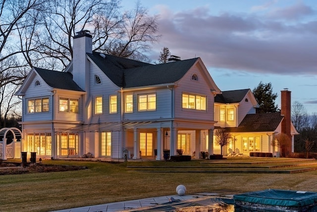 back house at dusk featuring a lawn