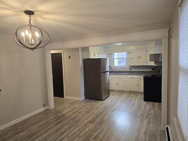 kitchen with stainless steel fridge, wood-type flooring, an inviting chandelier, white cabinetry, and black / electric stove