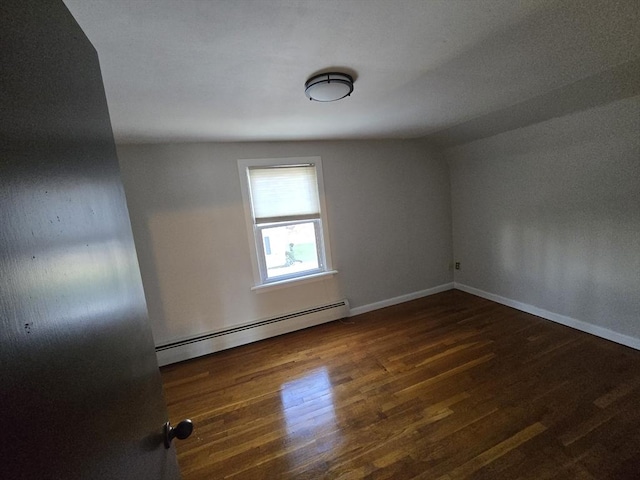 unfurnished room with vaulted ceiling, dark hardwood / wood-style flooring, and a baseboard heating unit