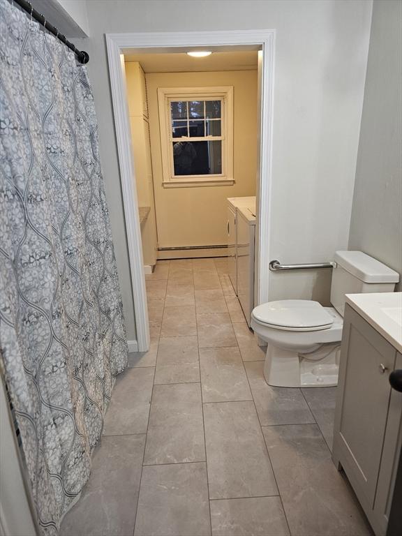 bathroom featuring baseboard heating, separate washer and dryer, tile patterned flooring, toilet, and vanity