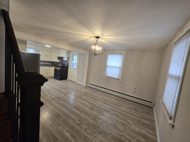 interior space with a baseboard heating unit, white cabinets, light wood-type flooring, appliances with stainless steel finishes, and a chandelier