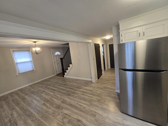 kitchen with stainless steel refrigerator, white cabinetry, a notable chandelier, pendant lighting, and light wood-type flooring