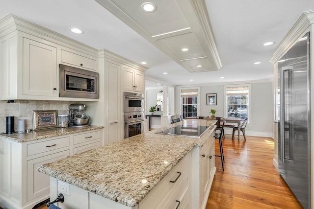 kitchen featuring light wood-type flooring, a breakfast bar, backsplash, a kitchen island, and built in appliances