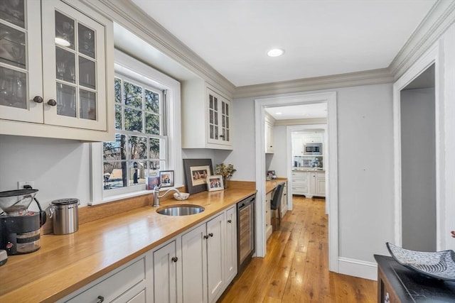 kitchen with stainless steel microwave, beverage cooler, ornamental molding, light wood-style flooring, and a sink