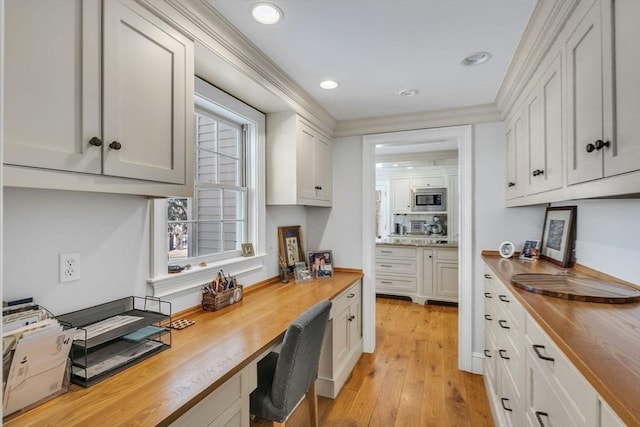 kitchen featuring white cabinets, built in desk, wood counters, stainless steel microwave, and light wood-type flooring