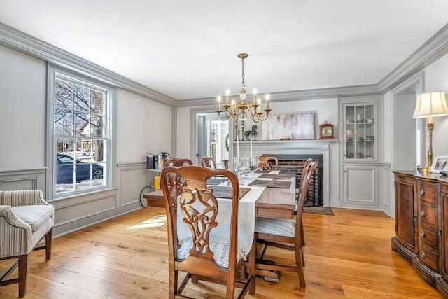 dining room featuring light wood-style flooring, ornamental molding, an inviting chandelier, wainscoting, and a decorative wall