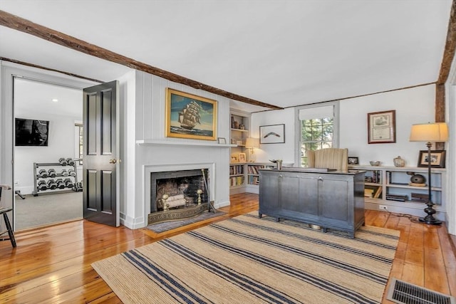 living room featuring a fireplace with flush hearth, light wood-type flooring, and visible vents