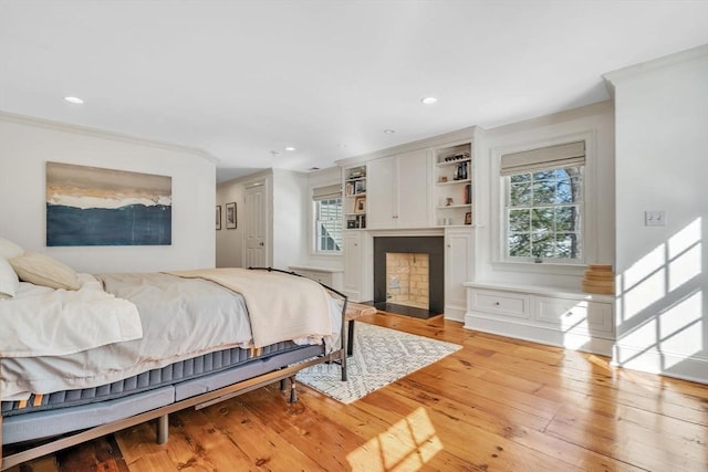 bedroom with crown molding, light wood-style flooring, a fireplace with flush hearth, and recessed lighting