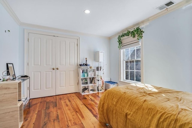 bedroom with light wood-style floors, visible vents, a closet, and ornamental molding