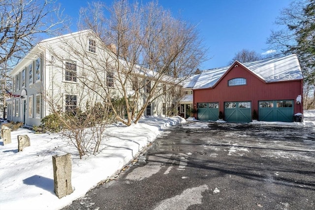 view of snow covered exterior featuring a barn, an outbuilding, and a garage