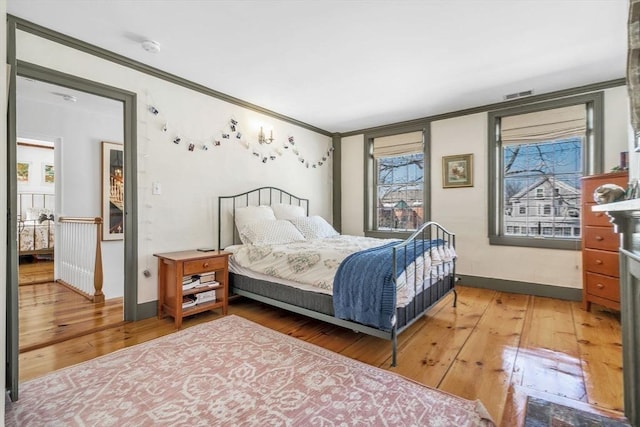 bedroom featuring hardwood / wood-style floors, baseboards, visible vents, and ornamental molding