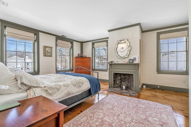 bedroom with crown molding, a fireplace with flush hearth, wood finished floors, and baseboards