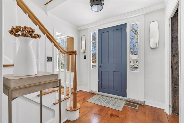 foyer with visible vents, ornamental molding, baseboards, and wood finished floors