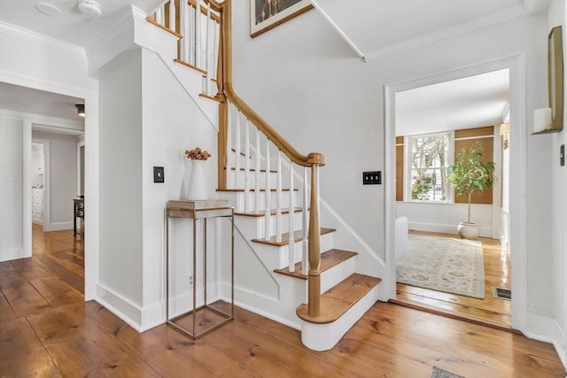 stairs featuring hardwood / wood-style floors, baseboards, visible vents, and ornamental molding