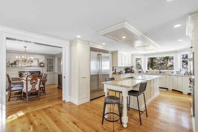 kitchen with light wood finished floors, a center island, a breakfast bar, ornamental molding, and built in fridge