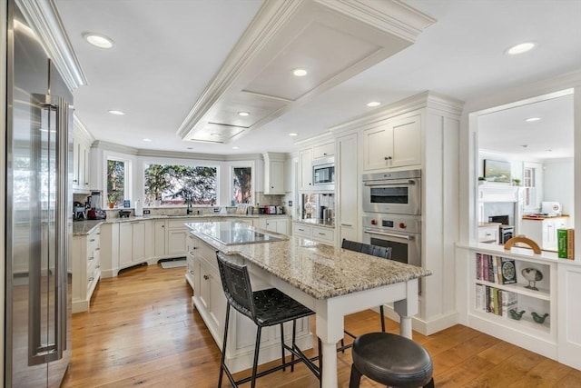 kitchen with a breakfast bar area, light wood finished floors, white cabinets, built in appliances, and a center island