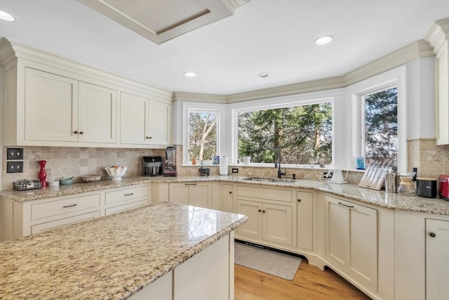 kitchen with backsplash, light stone countertops, light wood-style floors, and a sink