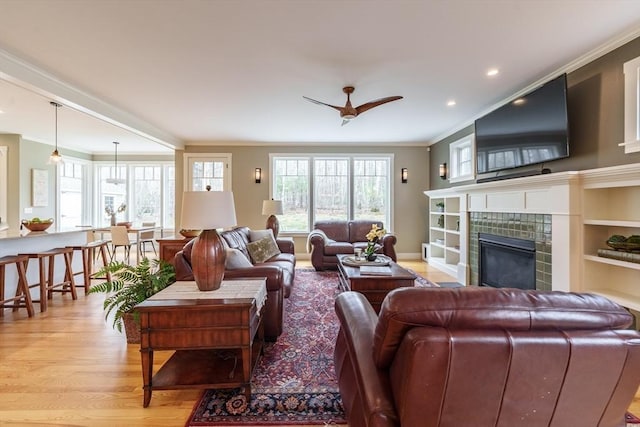 living area with crown molding, ceiling fan, light wood-style floors, recessed lighting, and a tile fireplace