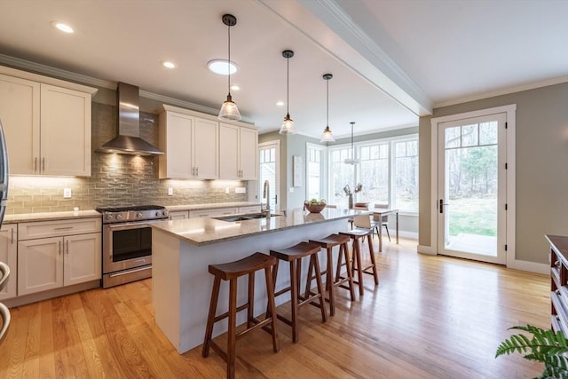 kitchen with wall chimney range hood, gas range, tasteful backsplash, a sink, and ornamental molding