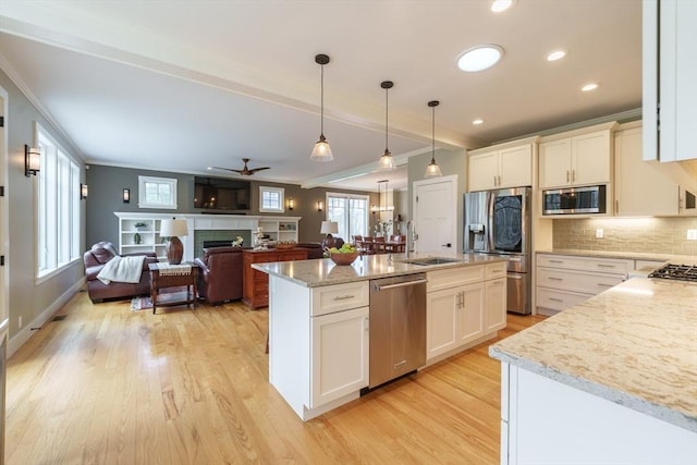 kitchen featuring appliances with stainless steel finishes, a sink, light wood-style floors, decorative backsplash, and ornamental molding