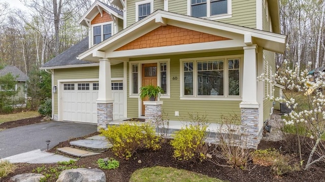 view of front facade with a garage, aphalt driveway, covered porch, a shingled roof, and central AC unit
