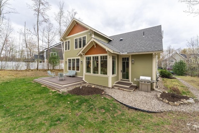rear view of house featuring roof with shingles, fence, a yard, and a deck