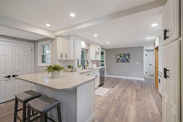 11 Rose Ave, Westport, MA 02790 - kitchen featuring dishwasher, a breakfast bar area, a peninsula, white cabinets, and light wood finished floors
