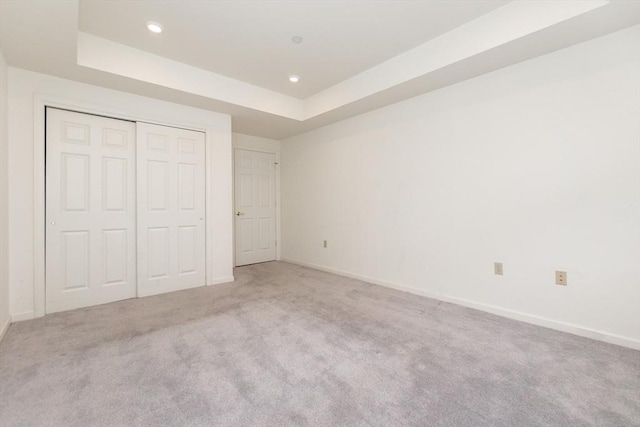 unfurnished bedroom with light carpet, a raised ceiling, and a closet